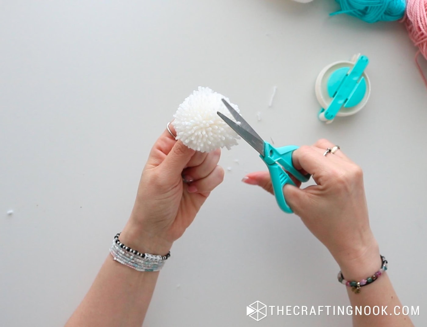 close view of the pompom and scissors cutting the excess to give the round shape of the pompom
