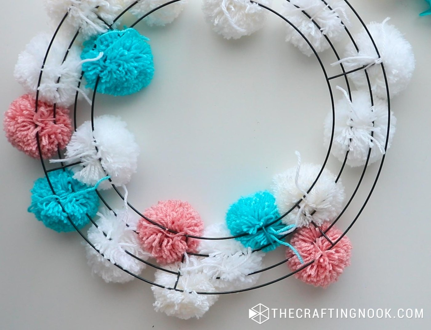 close up image of wire wreath with several pompoms already tied