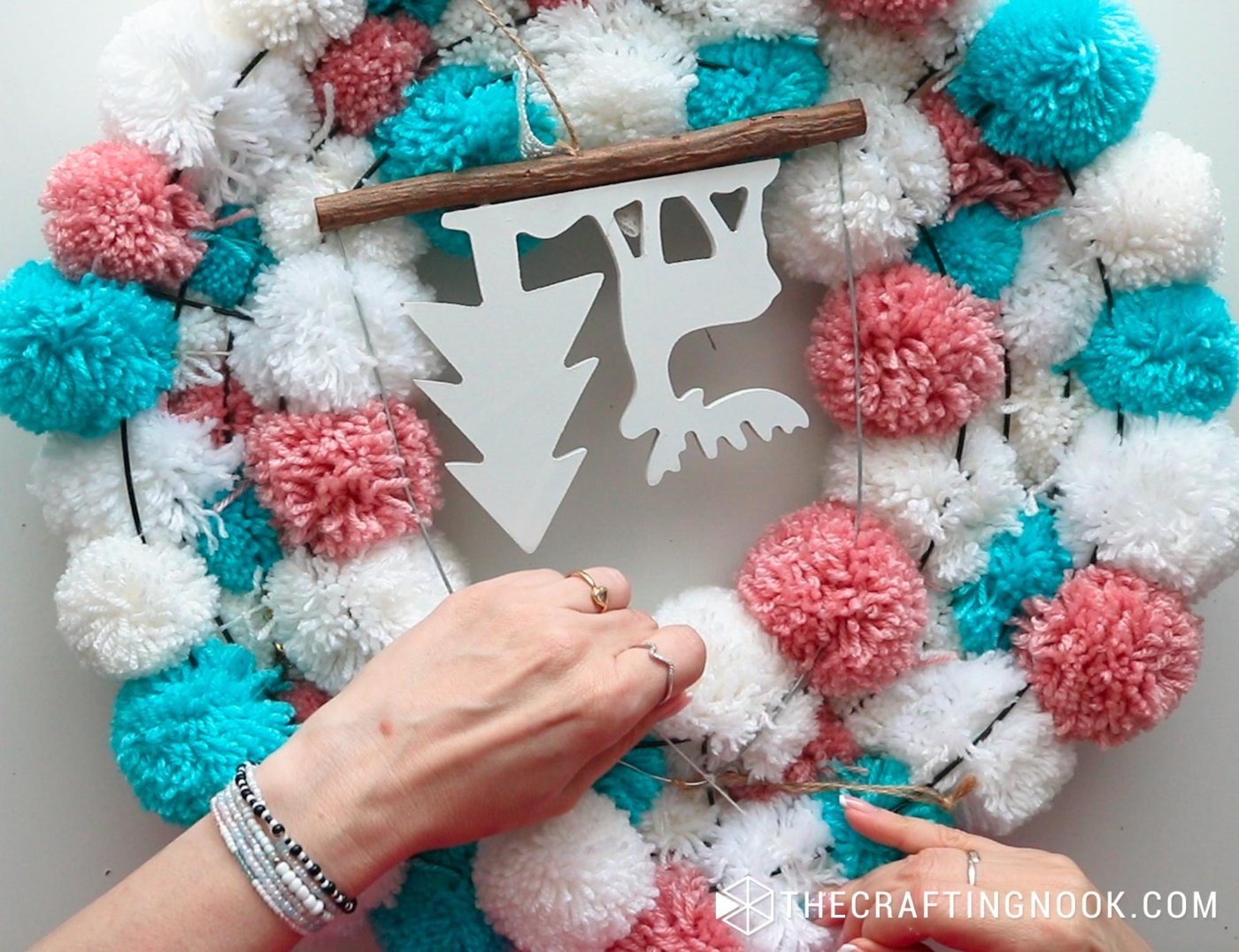 close up image tying the back of the pompom garland the deer hanger in the center
