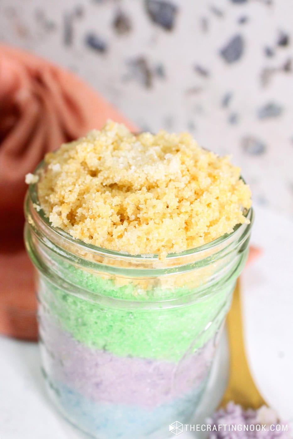 Closeup of the jar layers of sugar scrub in different pastel colors, blue, purple, green and yellow.