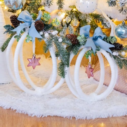 Two completed large hoop ornaments displayed under a Christmas tree decorated in whites, pinks, blues, and greenery. Feature image