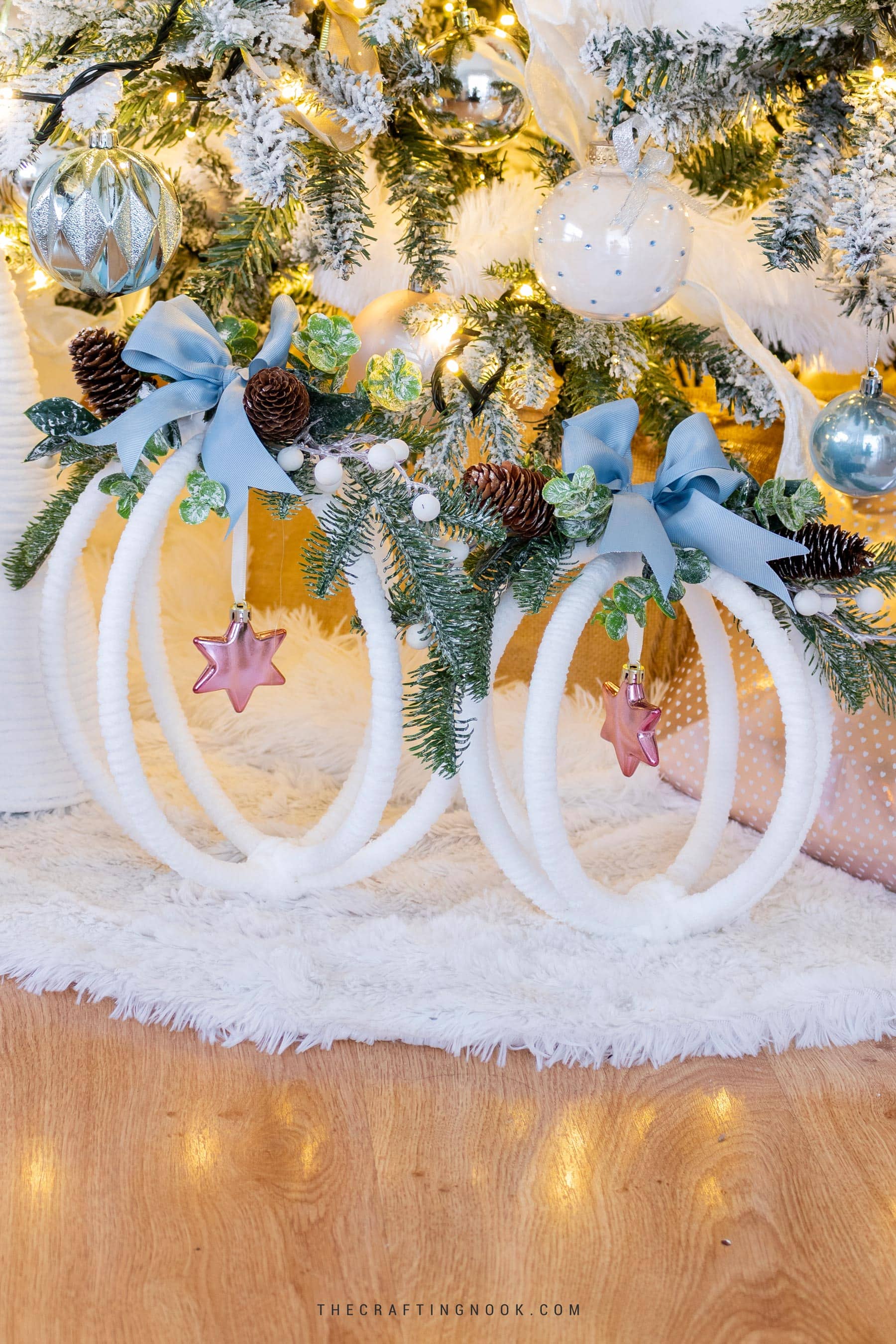 Two completed large hoop ornaments displayed under a Christmas tree decorated in whites, pinks, blues, and greenery. Feature image