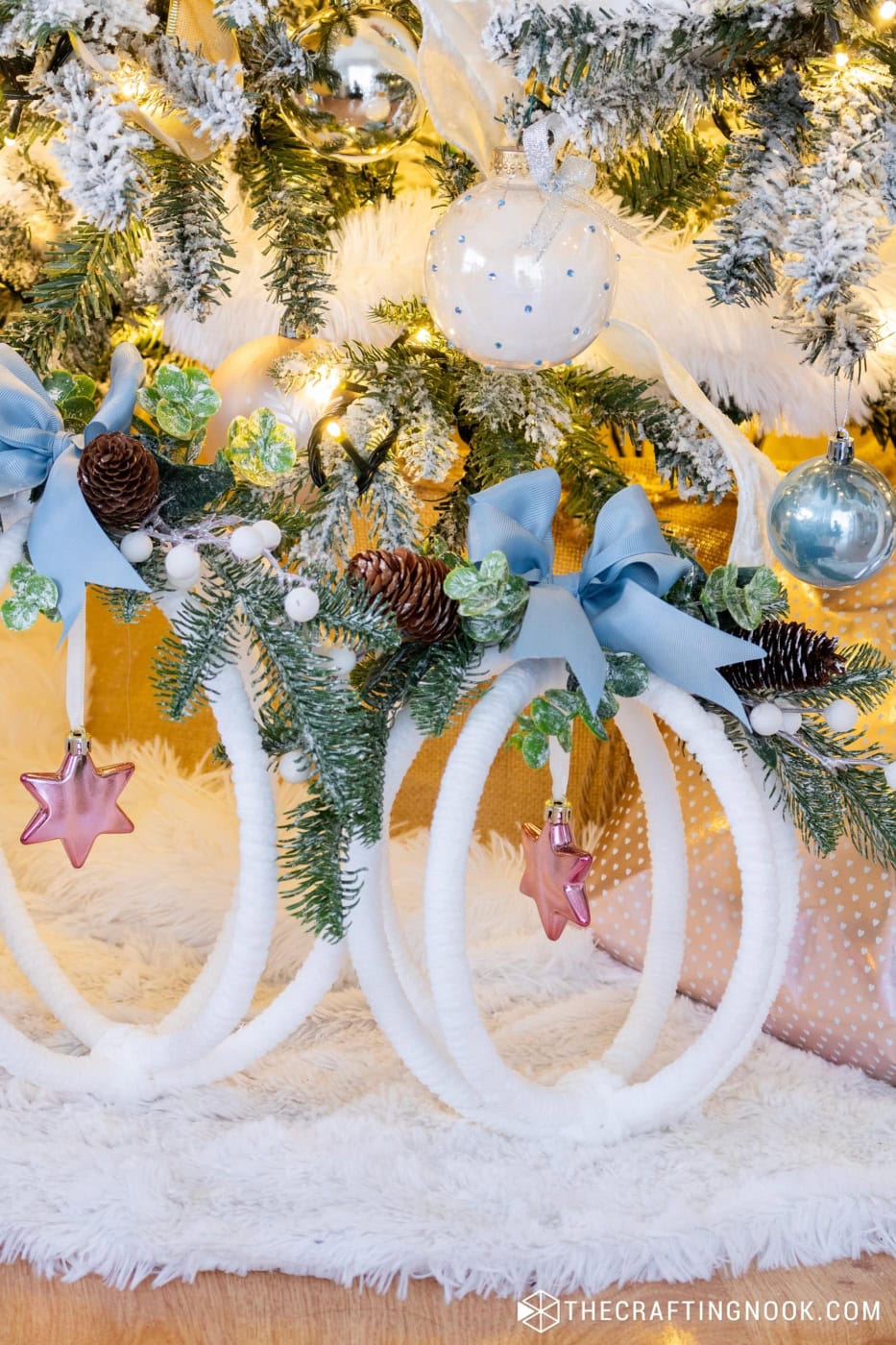 Two completed large hoop ornaments displayed under a Christmas tree decorated in whites, pinks, blues, and greenery but closer view of the smaller one