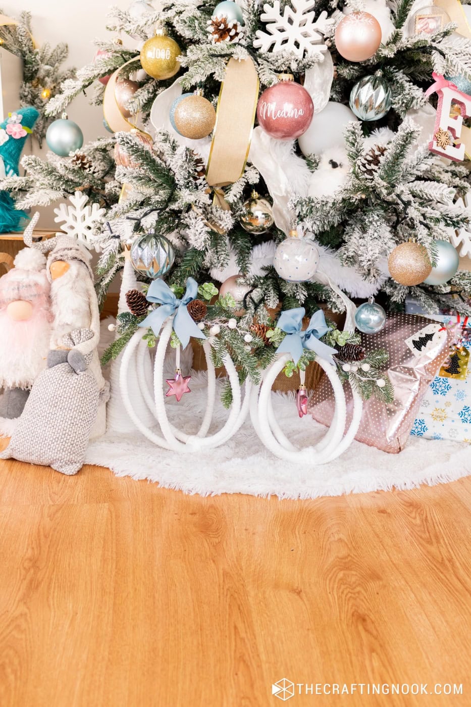 Two completed large hoop ornaments displayed under a Christmas tree decorated in whites, pinks, blues, and greenery.