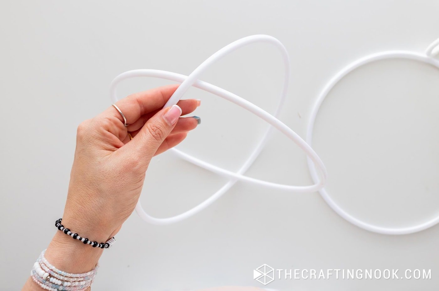 A hand holding two white hoops crossed together to form the base shape of the ornament.