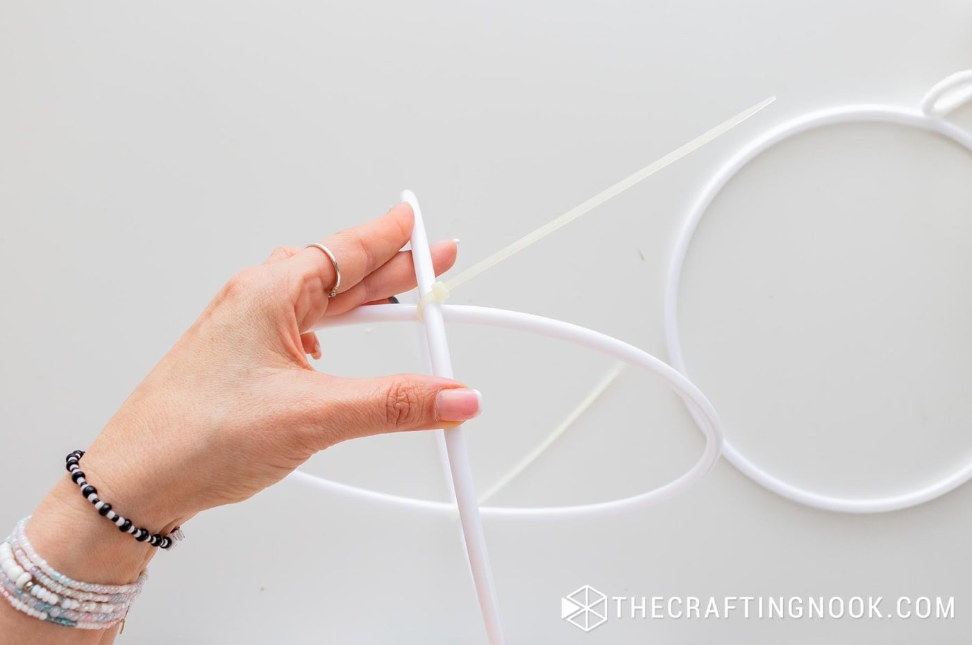 A hand adding a zip tie to secure two hoops together at the intersection.