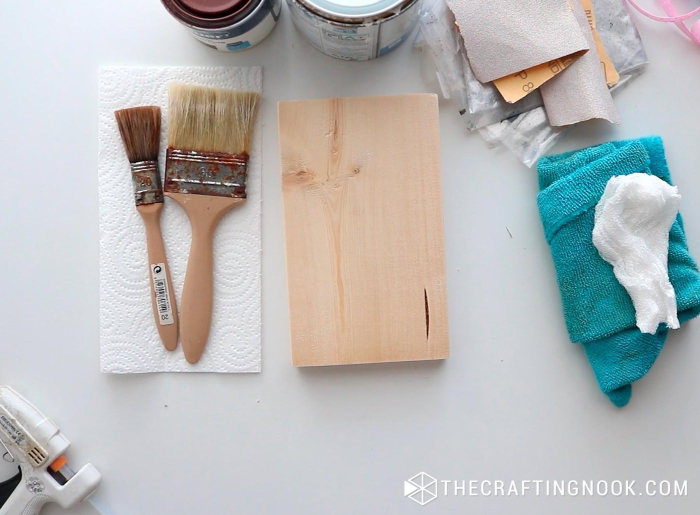 Supplies laid out on a table including paintbrushes, wood stain, sandpaper, and a small wood block.