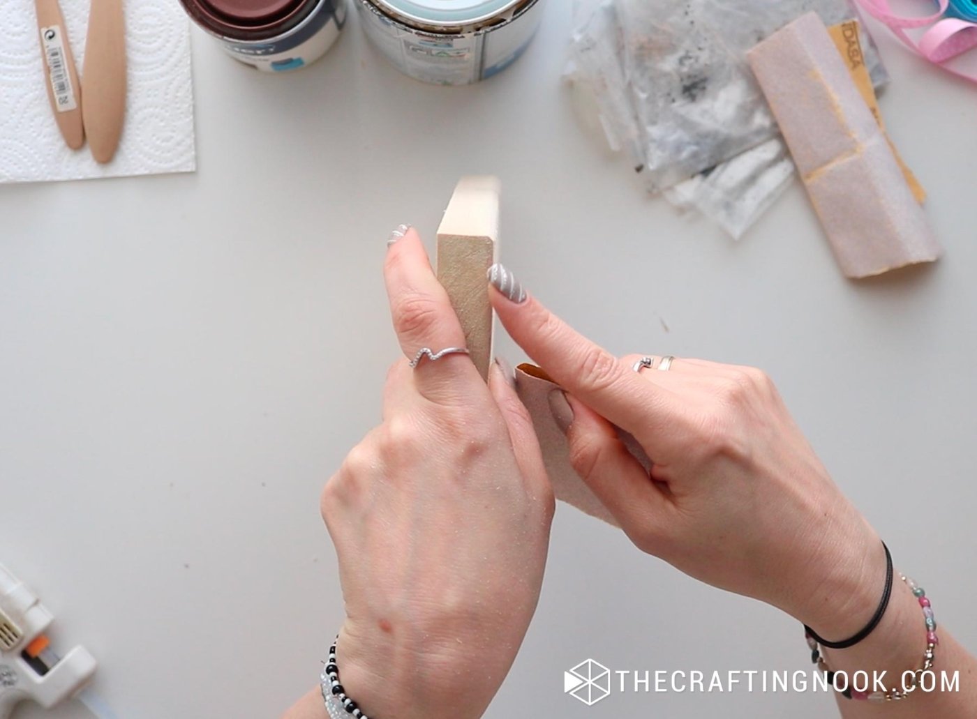 Hands sanding the edge of a wood block to shape the book spine.