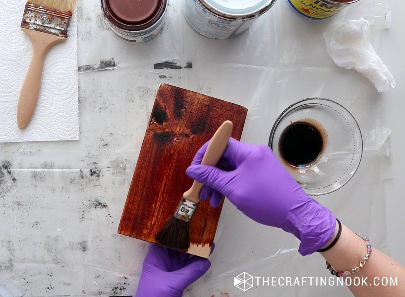 Applying dark wood stain to the block using a brush and wearing purple gloves.