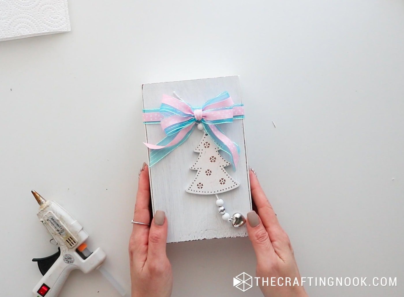 Finished wooden book stack decorated with a bow and small Christmas tree charm.