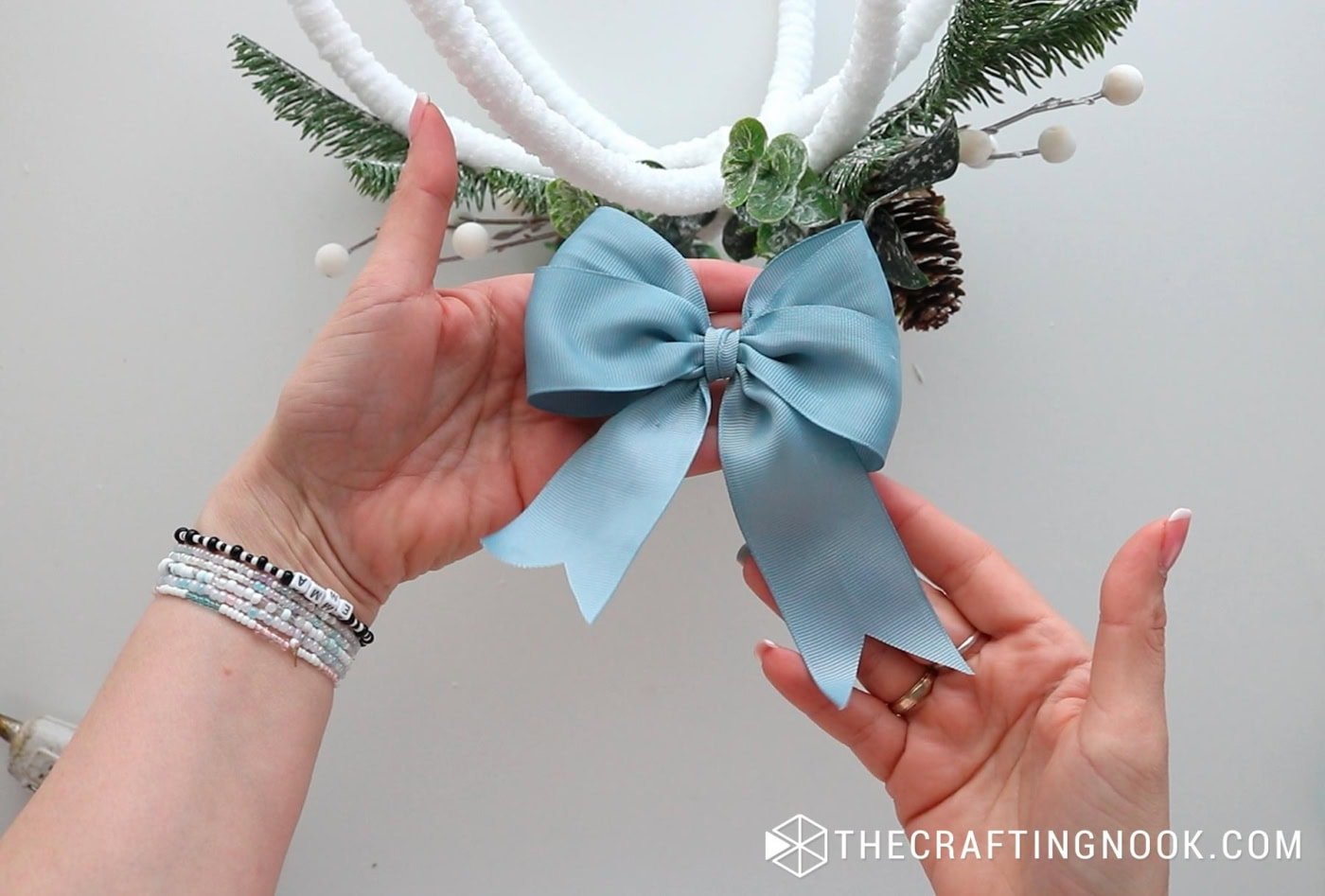 Hands holding a finished blue ribbon bow to be attached to the ornament.