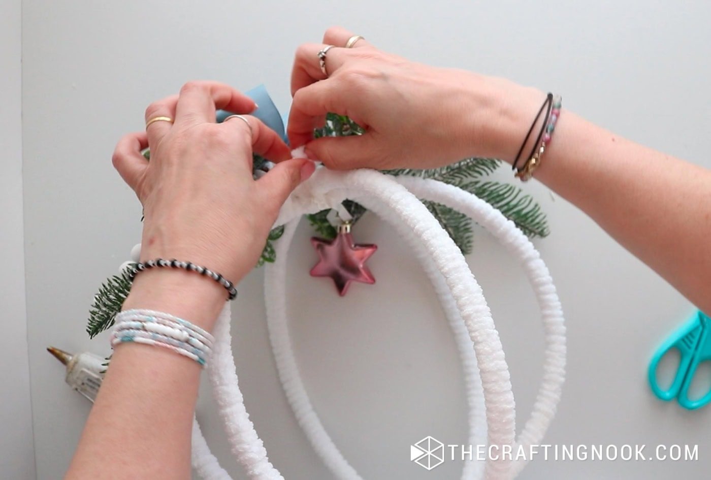 Attaching the small pink star ornament to the inside top of the hoop structure using yarn.