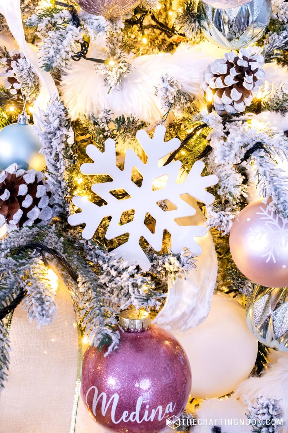 wooden snowflake ornament hanging on a snowy Christmas tree with gold accents.