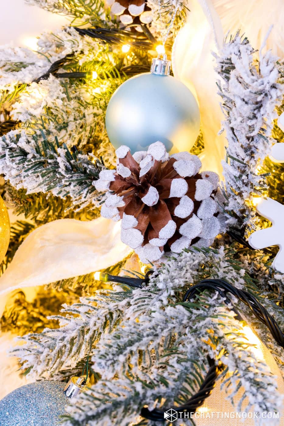 Close-up of flocked pinecone ornament on a tree with blue, pink and gold decorations.