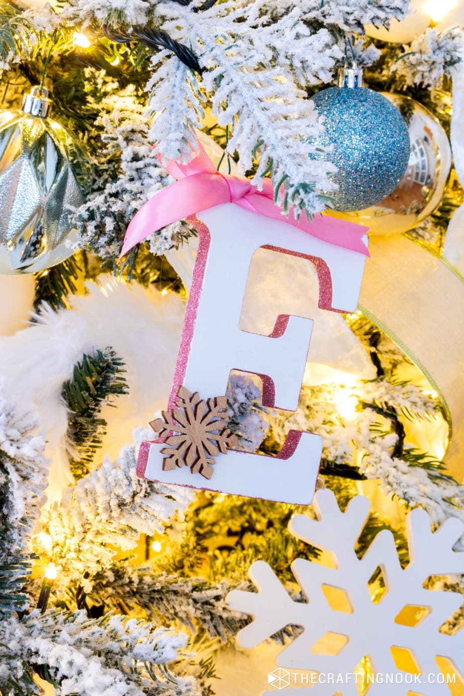 Handmade wooden monogram ornament hanging on a snowy Christmas tree with gold accents.