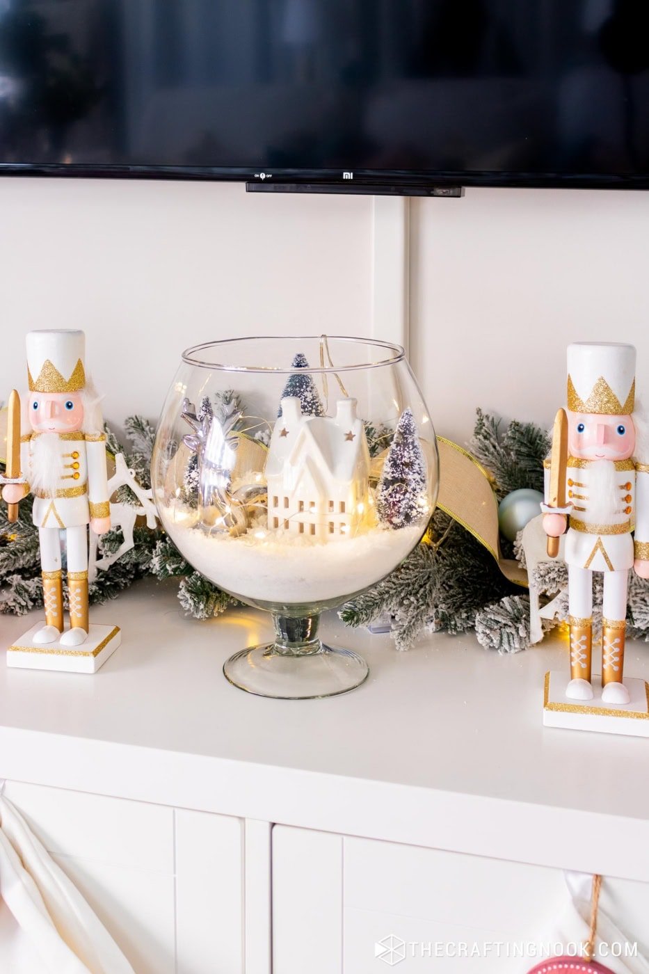 Finished winter scene in a glass vase displayed on a TV console with surrounding decor and 2 wooden nutcracker