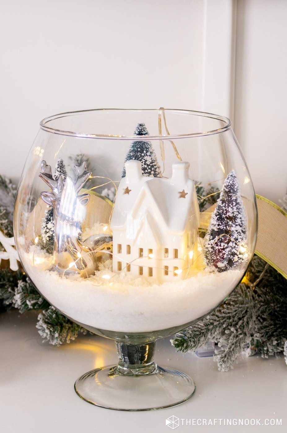 Finished winter scene in a glass vase displayed on a wooden surface with surrounding decor.