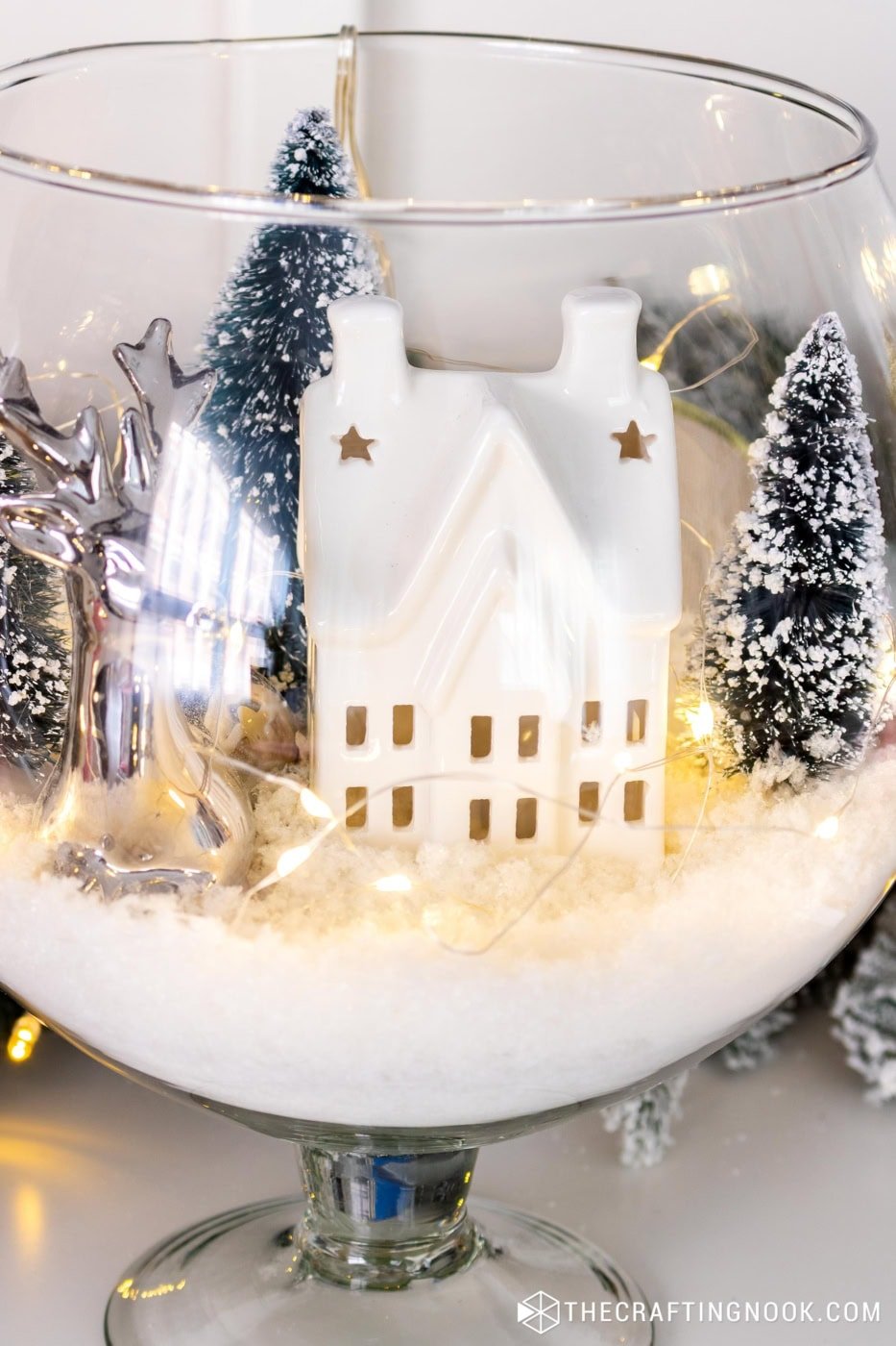 Close-up aesthetic shot of the final vase winter scene with a ceramic house, snowy trees, and warm lights.