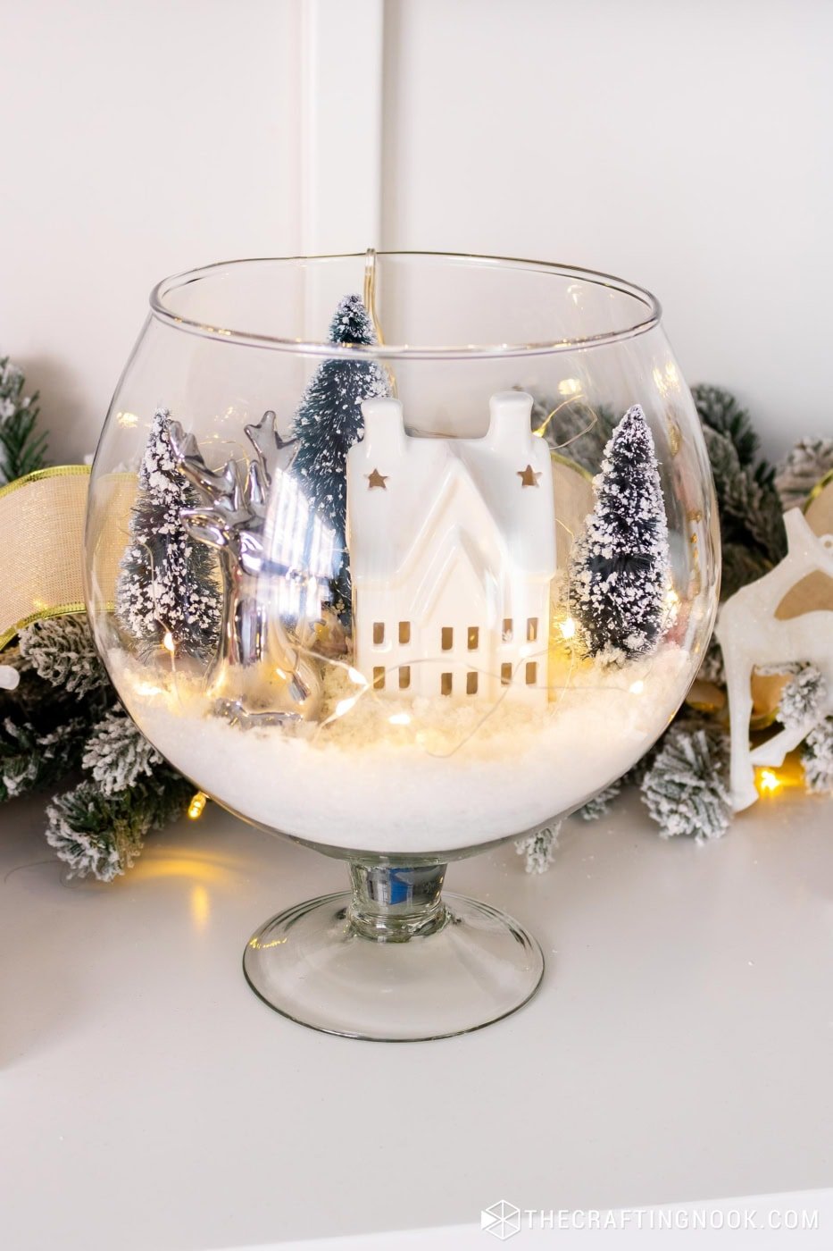 Angled view of the completed glass vase winter scene showing the ceramic house glowing from inside.