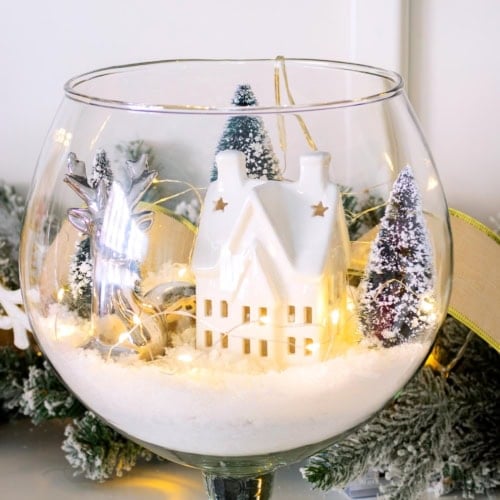 Finished winter scene in a glass vase displayed on a wooden surface with surrounding decor. Feature image.
