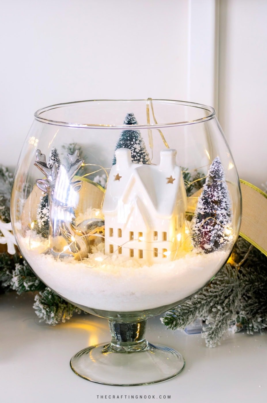 Finished winter scene in a glass vase displayed on a wooden surface with surrounding decor. Feature image.