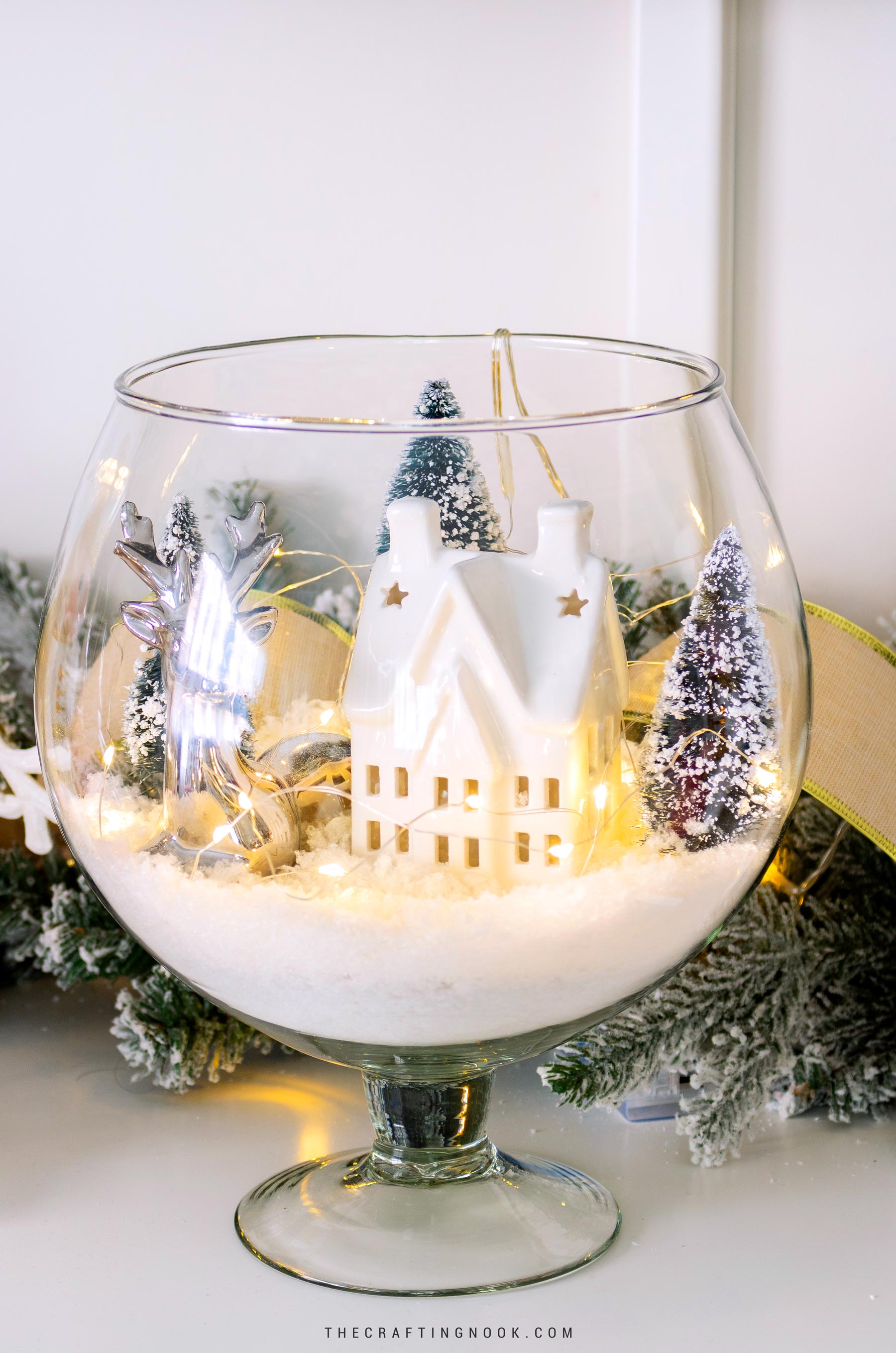 Finished winter scene in a glass vase displayed on a wooden surface with surrounding decor. Feature image.