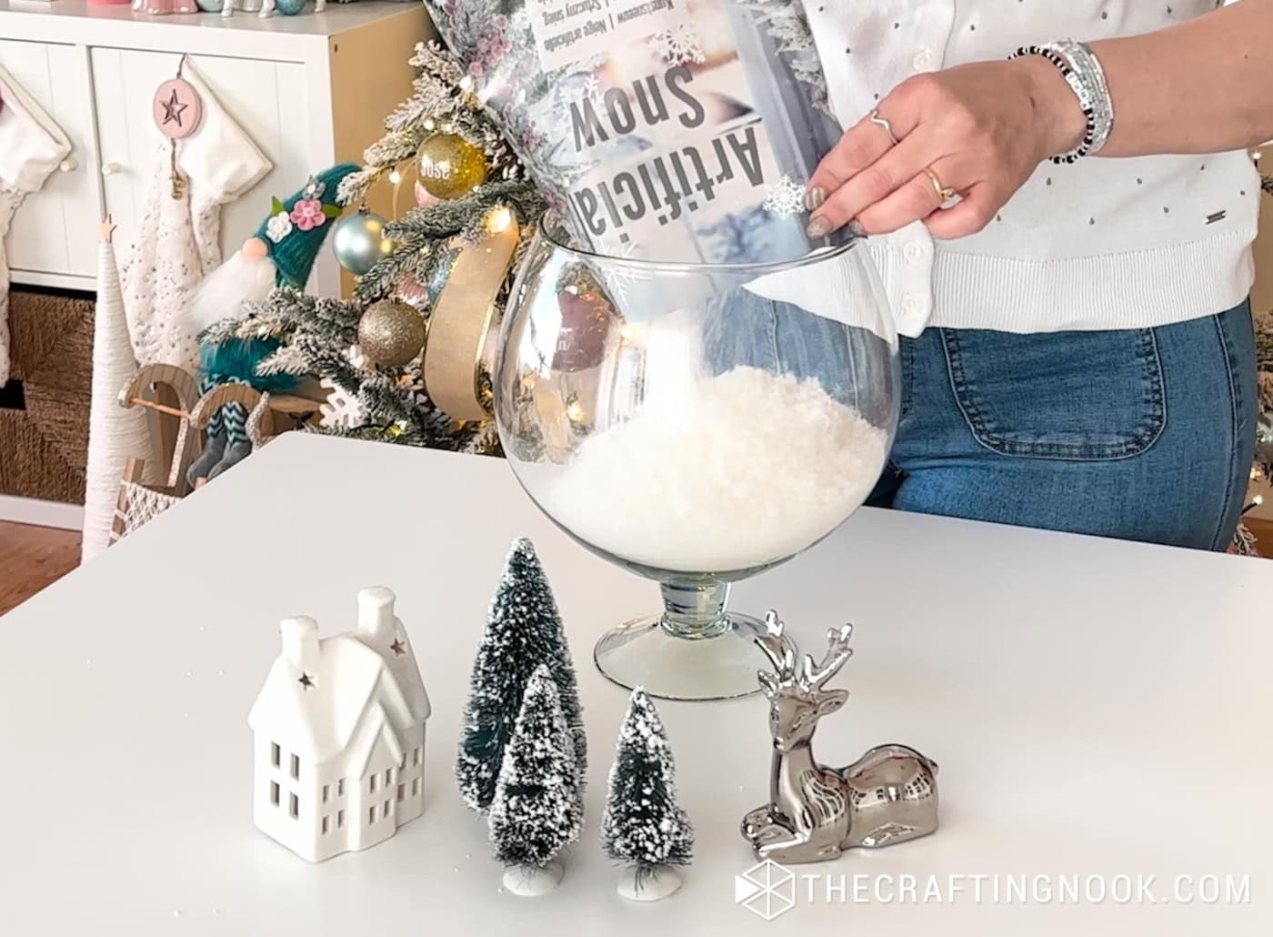Artificial snow being poured into the bottom of a tall glass vase to create the base of a winter scene.