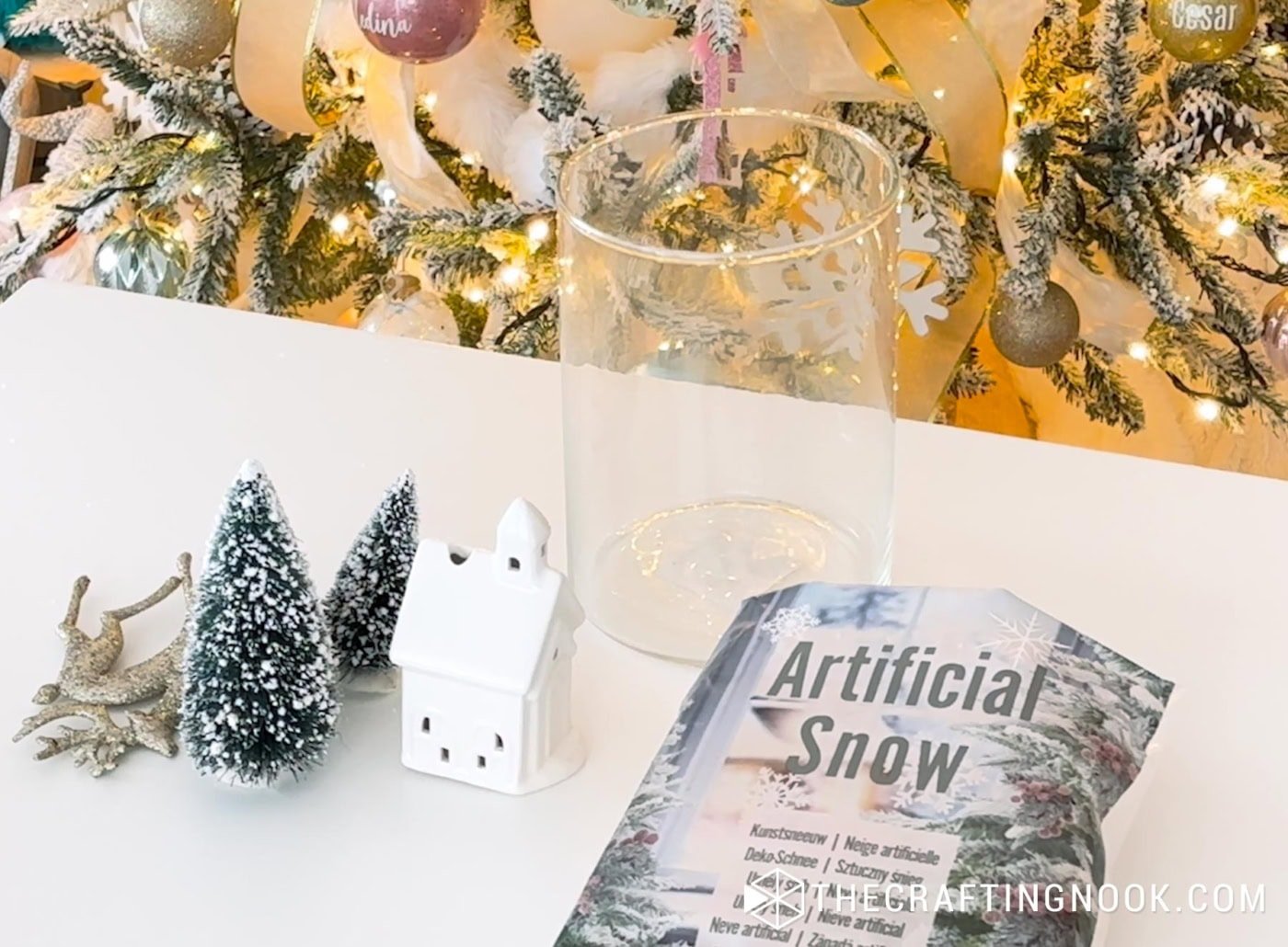 Tall cylinder jar filled with artificial snow, ceramic house, and bottle brush trees.