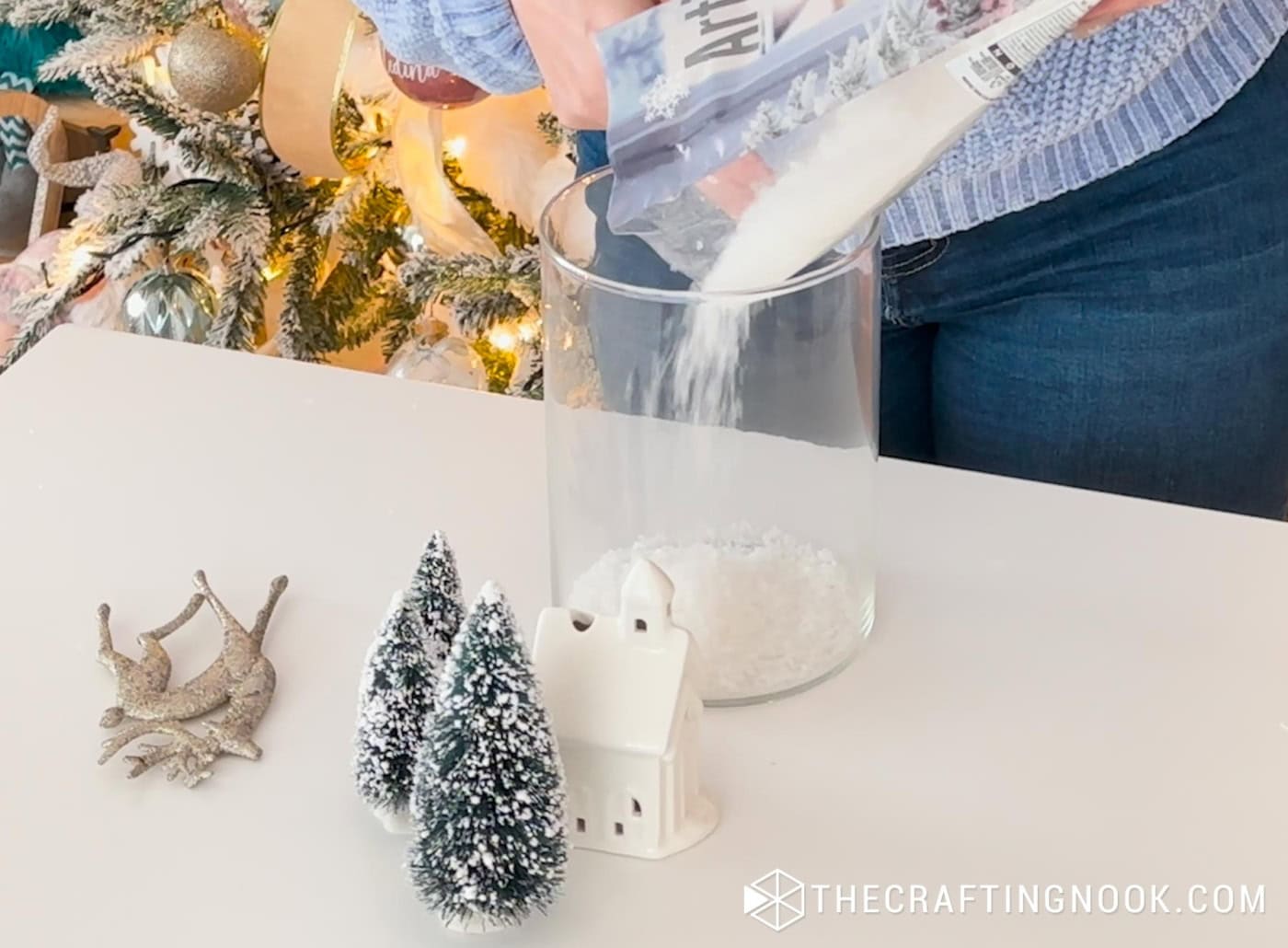 Artificial snow being poured into the bottom of a tall glass jar to create the base of a winter scene.