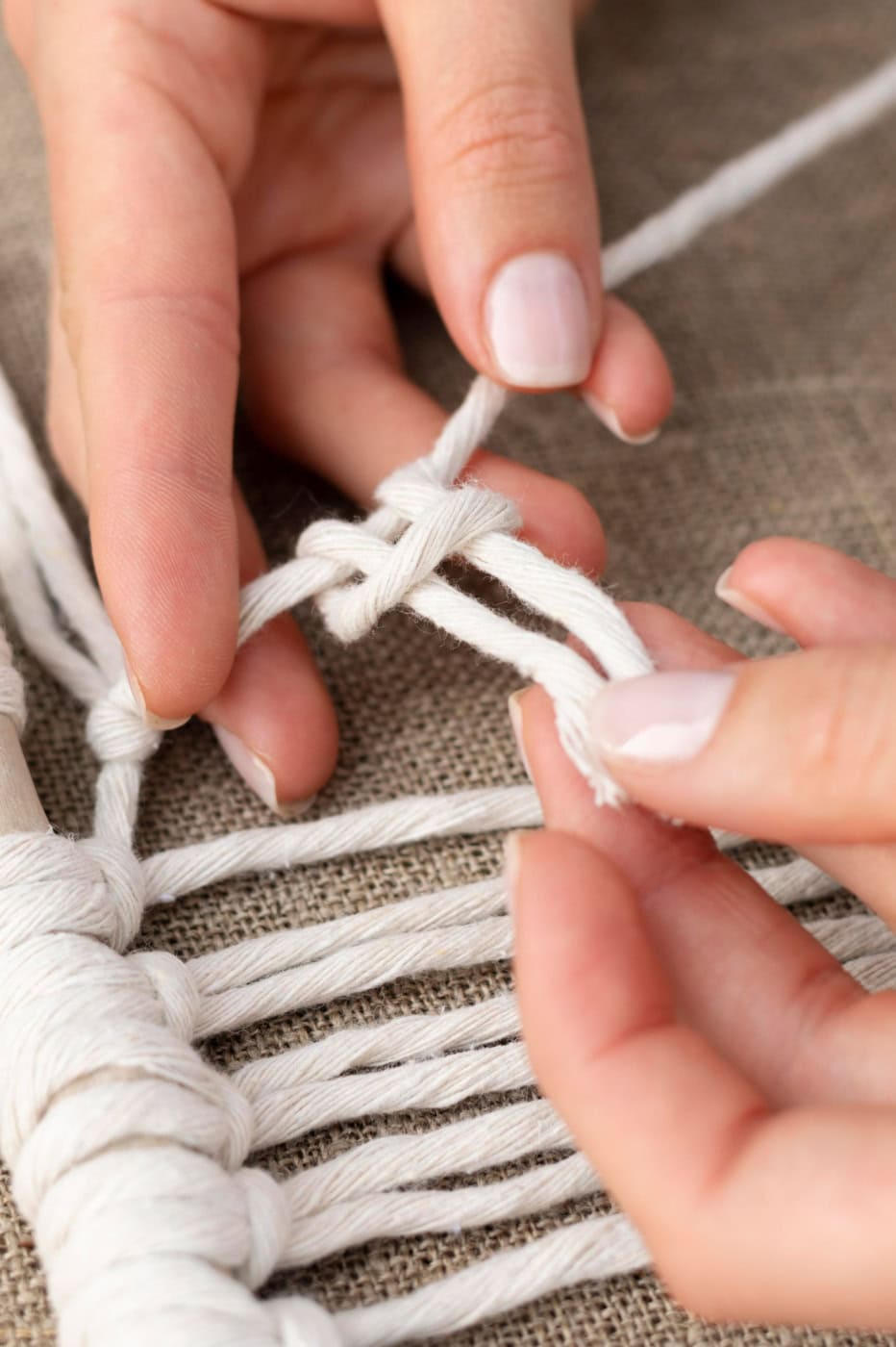 Hands tying a basic macrame knot with white cords for beginners.