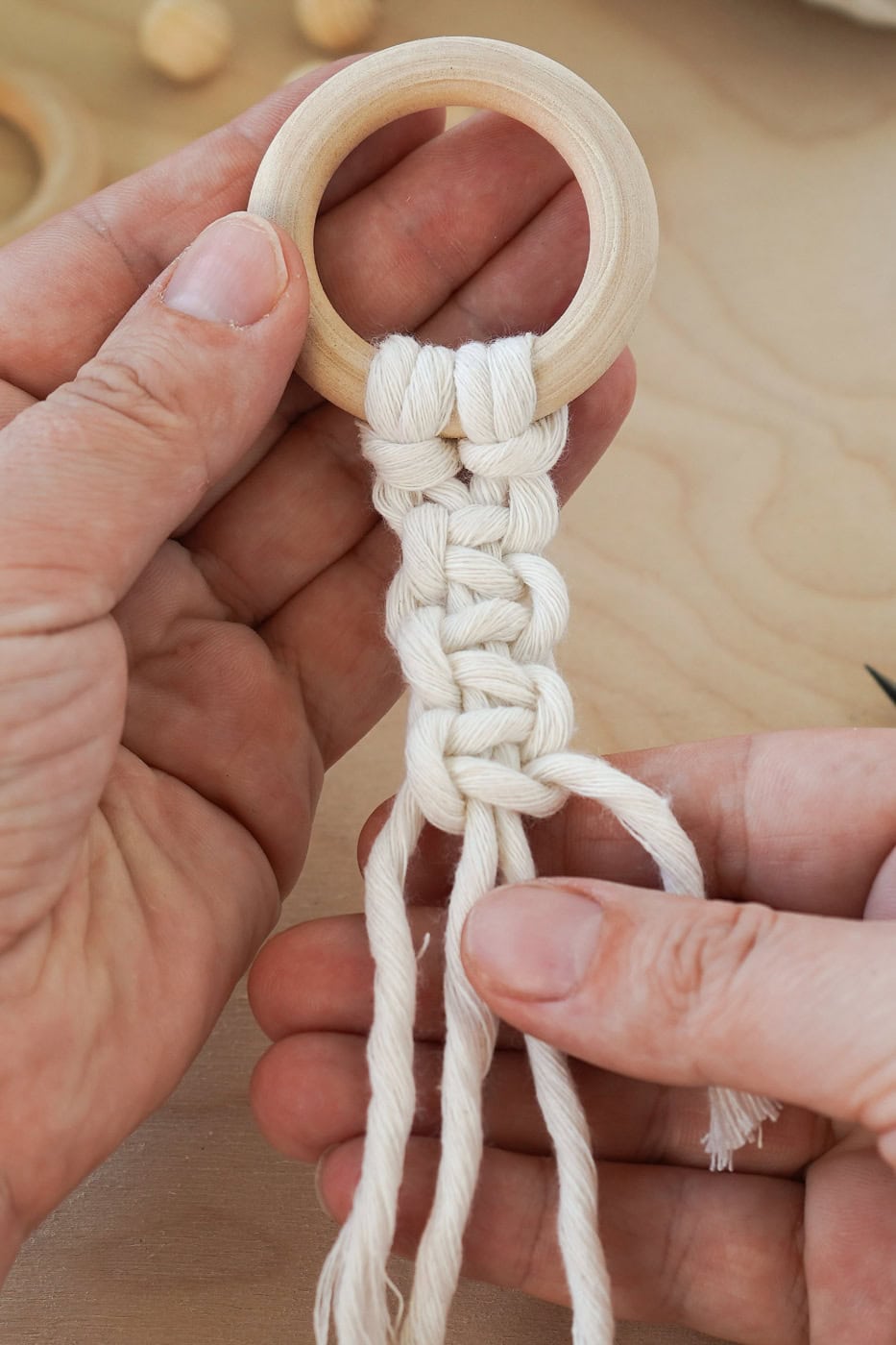 Hand tying a macrame knot with white cord and wooden ring for beginners.
