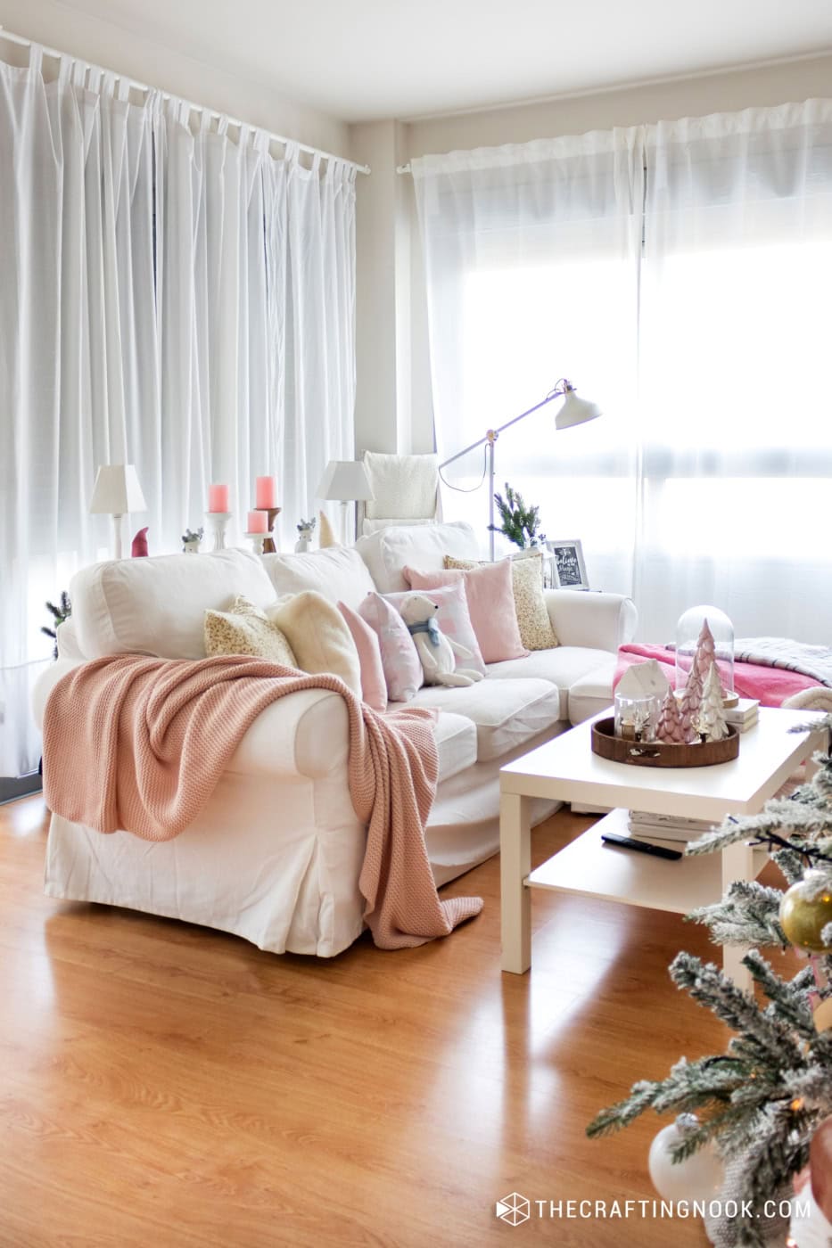 Bright living room with pastel pink and white accents, cozy throws, and natural light. Perfect for s.