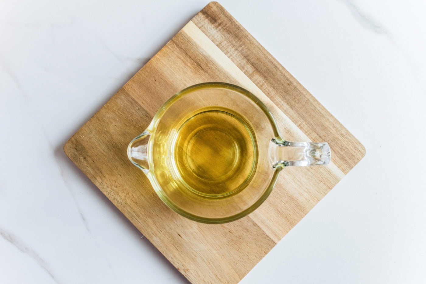 Melted soy wax in a glass measuring cup resting on a wooden board.