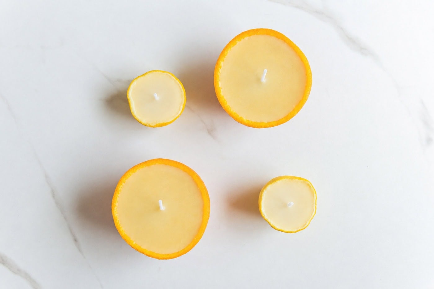 Hardened orange and lemon peel candles filled with soy wax and centered white wicks on a white marble surface.