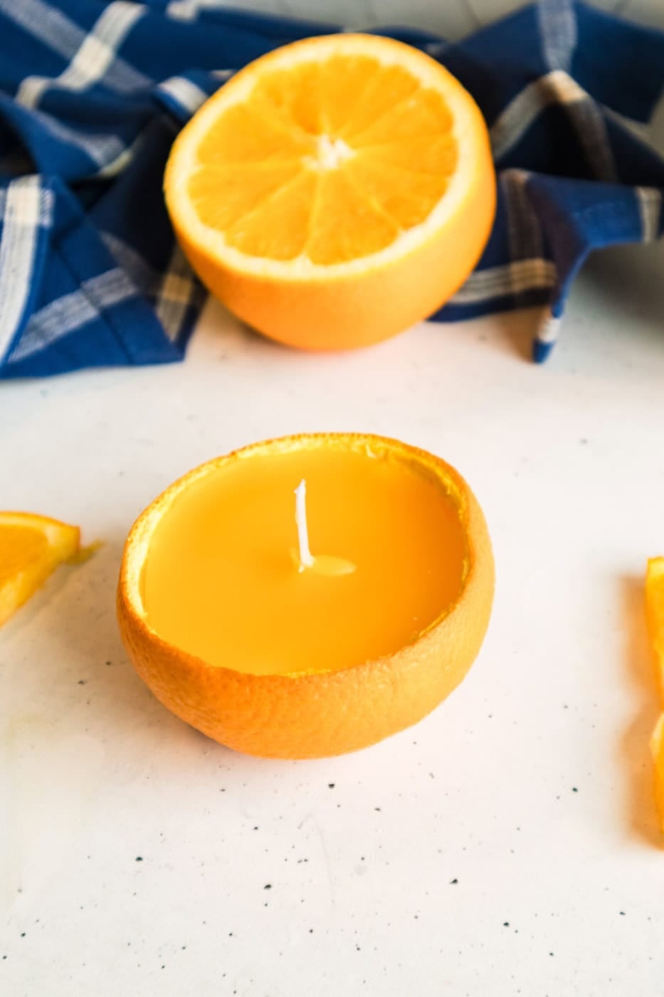 Vertical close-up of a finished orange peel candle with a centered wick and fresh orange half in the background.