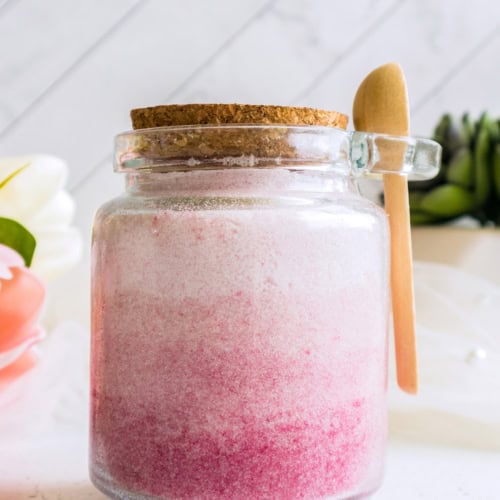 Pink ombre DIY body sugar scrub in glass jar with wooden spoon and cork lid.