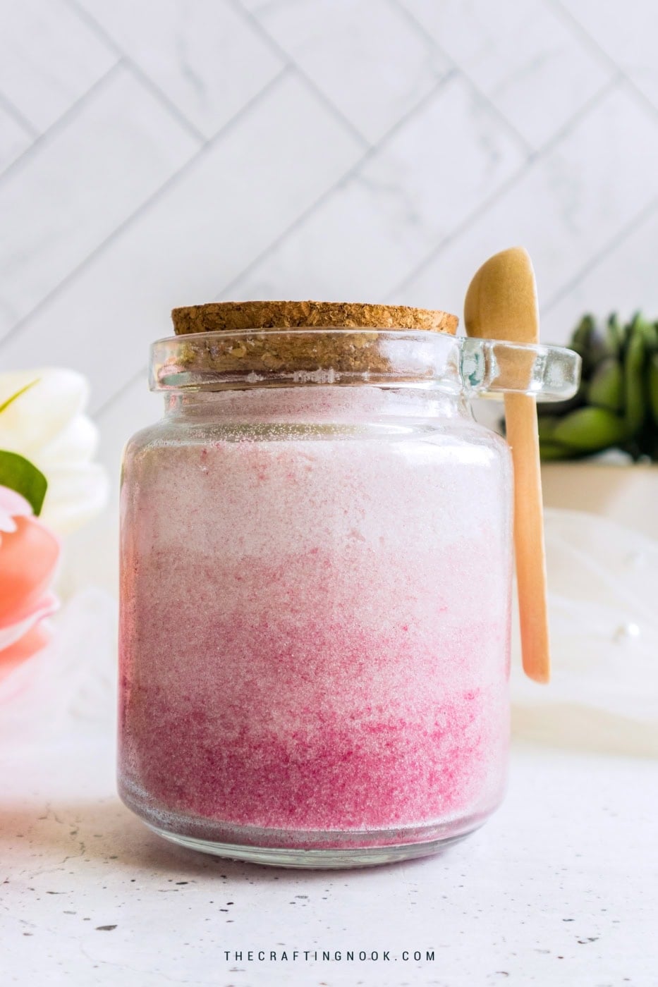 Pink ombre DIY body sugar scrub in glass jar with wooden spoon and cork lid.