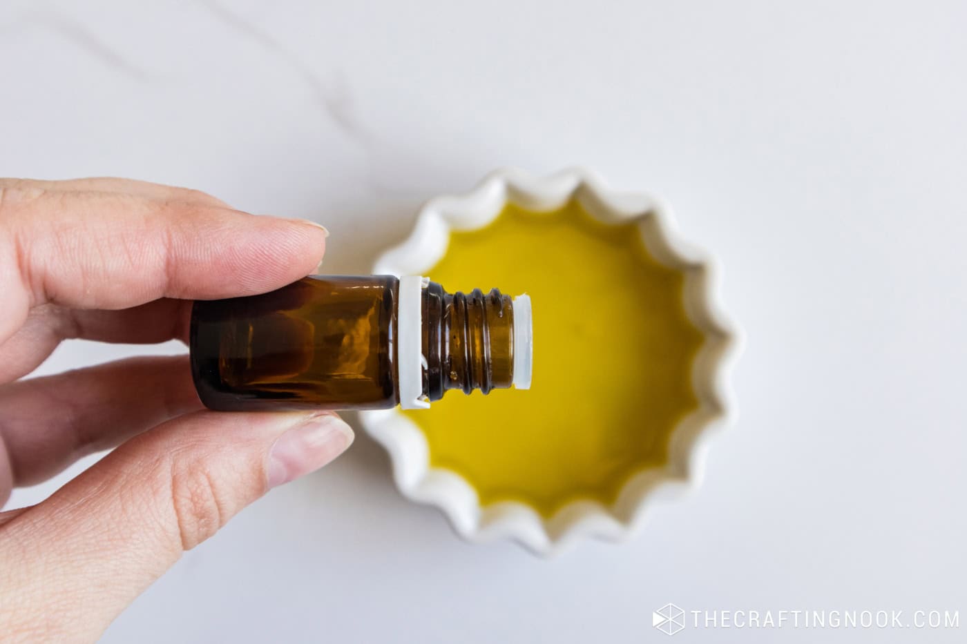 Hand holding an amber essential oil bottle over a small bowl of golden oil