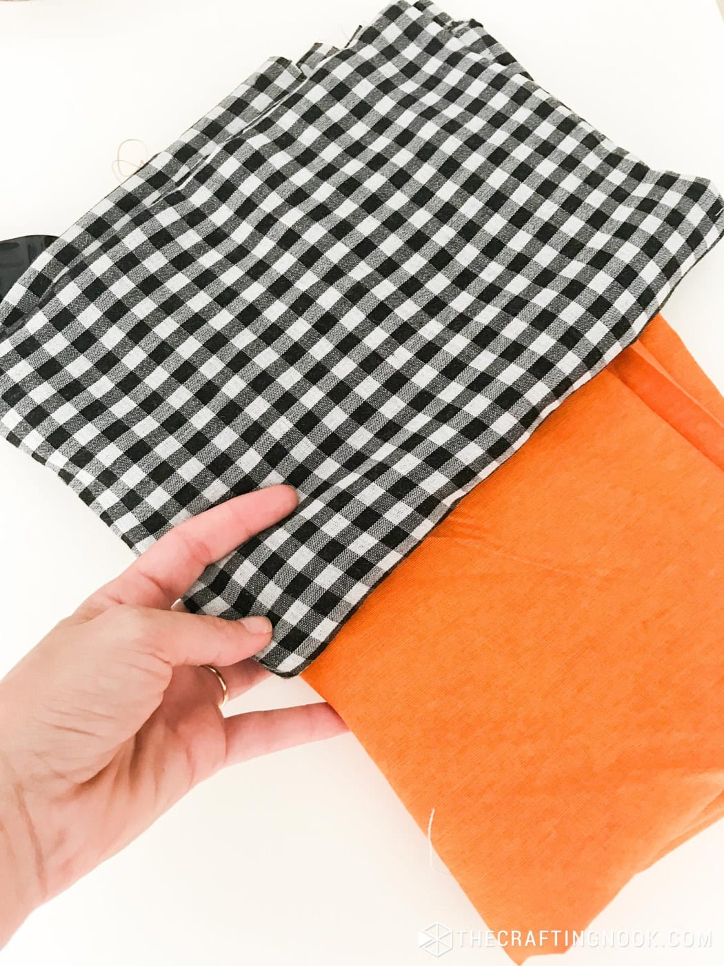 Hand holding folded black and white gingham fabric next to orange cotton fabric