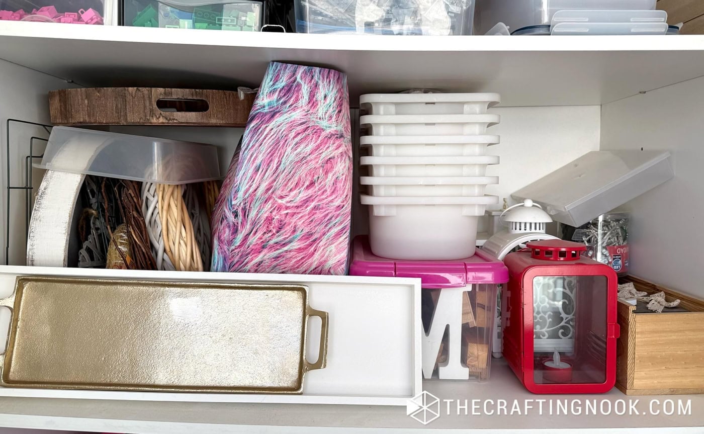 Craft closet shelf with yarn, stacked storage bins, a wood tray, and a small red lantern