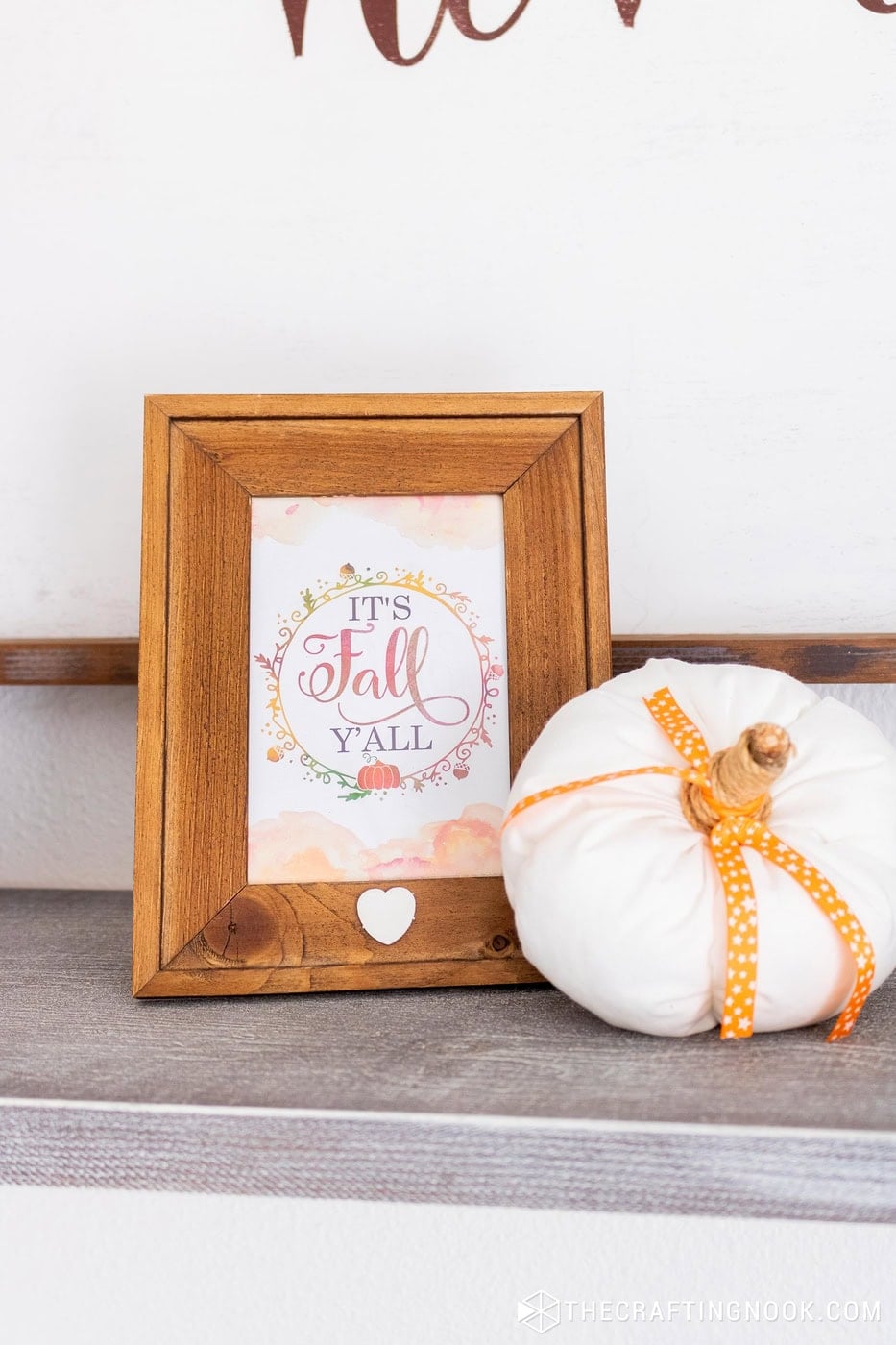 Framed "It's Fall Y'all" print next to a white fabric pumpkin with an orange ribbon