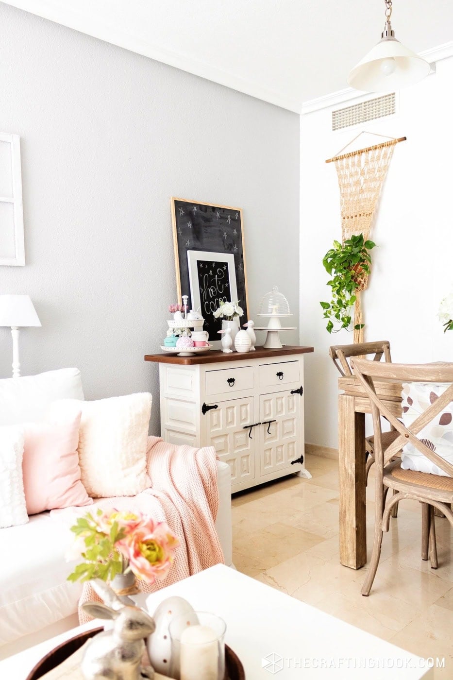 Living room corner with a white cabinet, a hot cocoa sign, and a macrame plant hanger