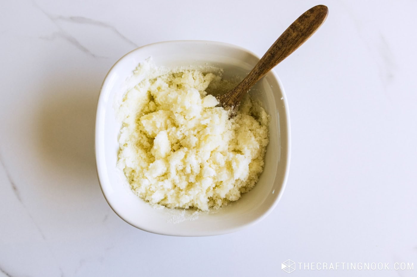 White sugar scrub base mixed in a white bowl with a wooden spoon