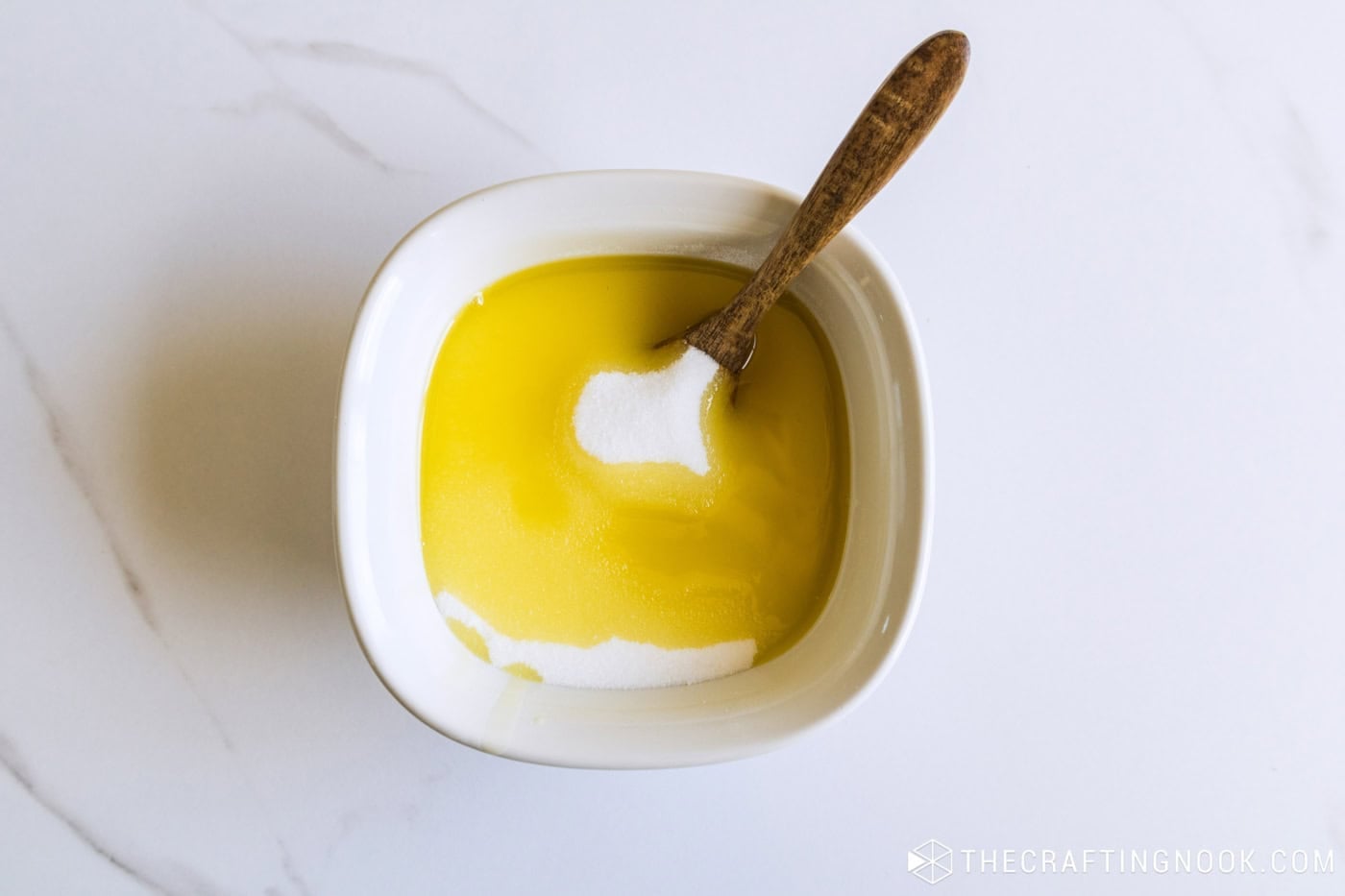 Bowl of sugar and golden oil not yet mixed, with a small wooden spoon resting in it