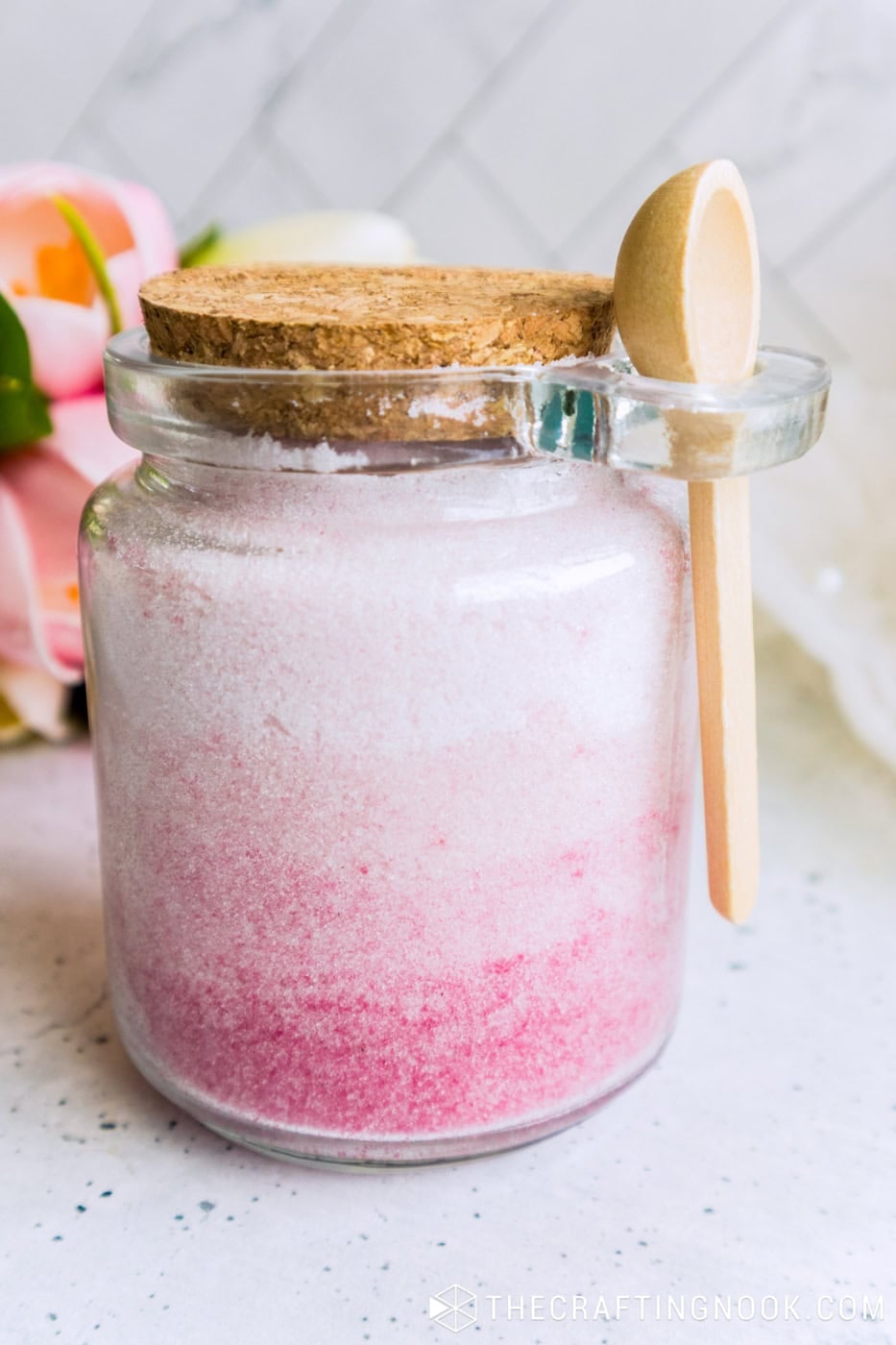 Close-up of a glass jar with cork lid, filled with sugar scrub that goes from white to bright pink