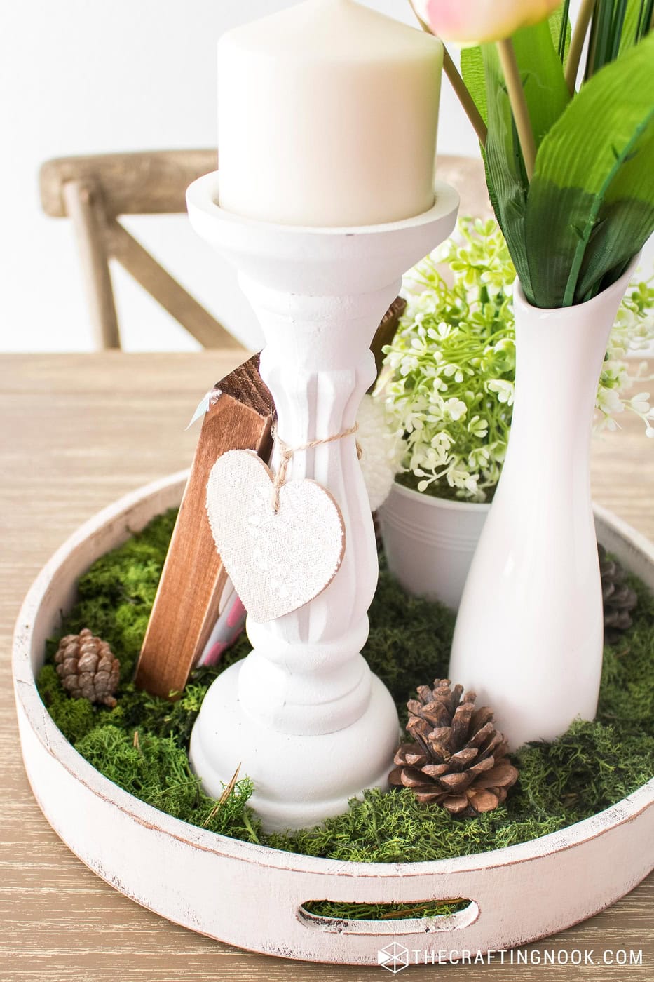 Spring centerpiece tray with a white candlestick, moss, pinecones, and faux flowers