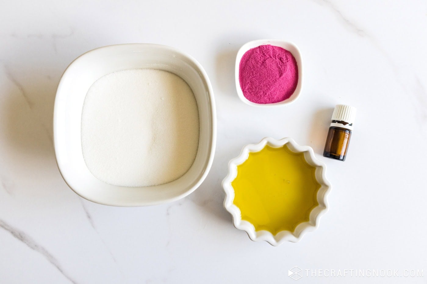 Ingredients for a pink ombre sugar scrub: white sugar, pink powder, oil and an essential oil bottle on a marble table