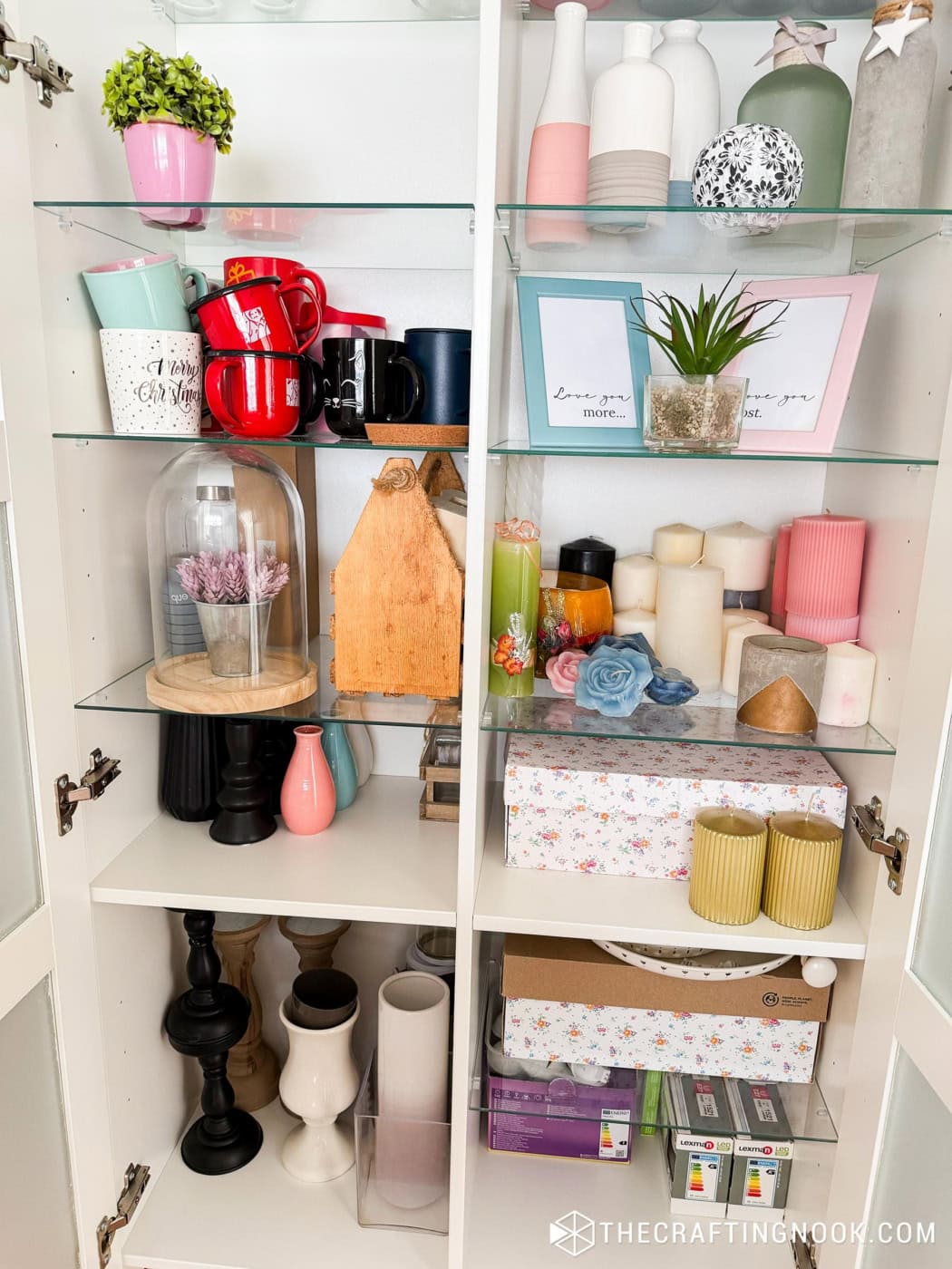 White glass cabinet storing vases, candles, mugs, and other home decor