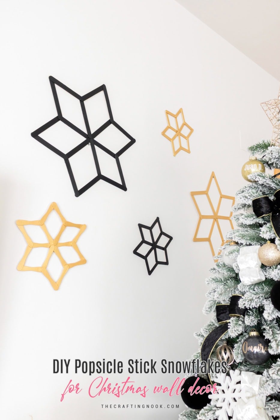 Five handmade black and gold popsicle stick snowflakes in different sizes arranged on a white wall.