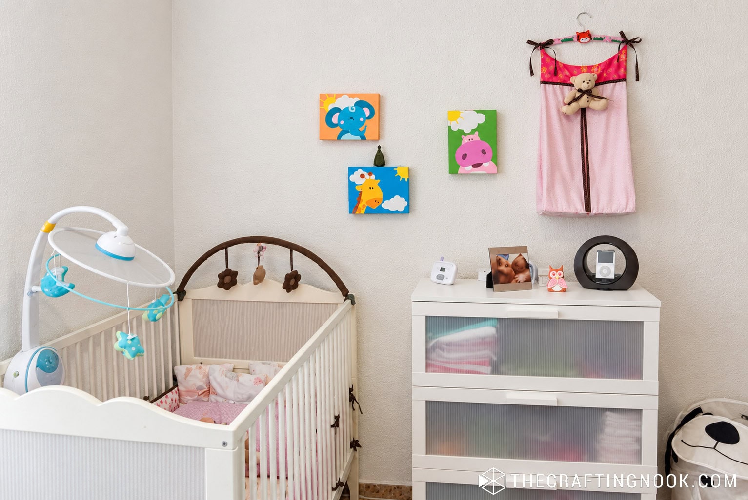 Baby nursery with crib, changing dresser, and handmade diaper stacker hanging on the wall
